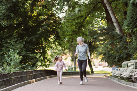 Family sports and outdoor activity concept. Cheerful young Muslim mother in hijab enjoying jogging together in park with her cute active little daughter. Mom and child jogging in the parkの写真素材