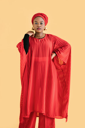 Portrait of charming pleasant African woman wearing red traditional red suit and turban, looking at...