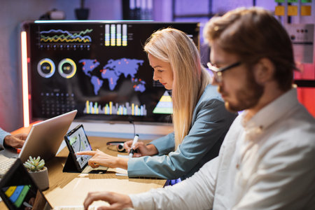 Side view of caucasian male and female financiers with modern gadgets on desk studying database of...