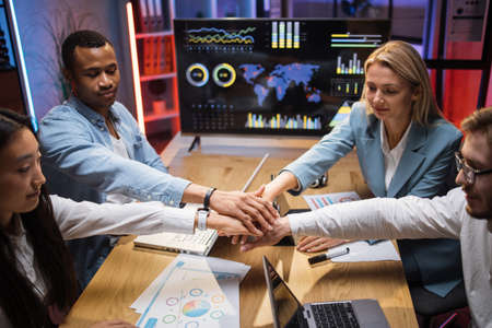 International team of competent office workers holding their hands together in circle after profitable cooperation at office room. Modern technology for work on desk. Teamwork concept.の写真素材