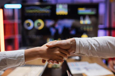 Close up of man and woman in white shirt shaking hands after meeting at office. Blur background of computer monitor with financial report. Concept of business, people, success and technology.の写真素材