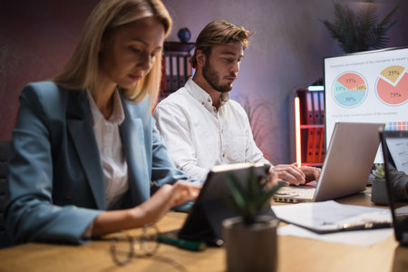 Caucasian man and woman in formal wear working on modern gadgets while sitting at desk. Two...