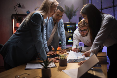 Group of international brokers standing around office table and analysing market reports. Four...