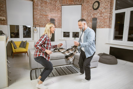 Joyful mature couple moving actively at home while spending free time together at home. Handsome man...
