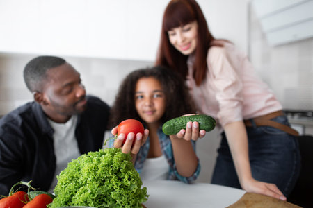 Tomato and cucumber. View of the happy multiracial family of three sitting at the kitchen and...