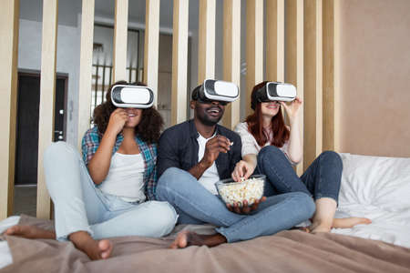 It is unbelievable. Excited african bearded dad, sitting with his family, european wife and daughter, watching movie in 3D virtual reality glasses for the first time and feeling excited.の写真素材