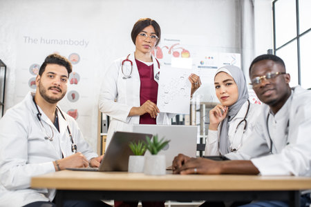 Professional medical specialists using modern laptops and tablets during conference at hospital. Multiracial doctors discussing important medical themes at boardroom.の写真素材