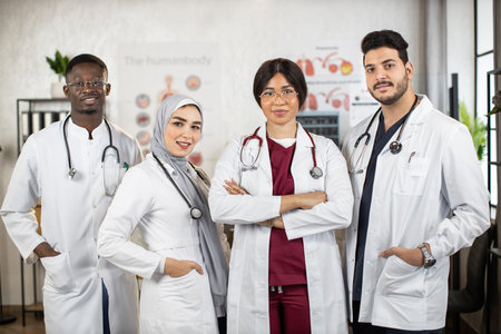 Team of female and male multiracial doctors in white lab coats keeping hands crossed or in the pockets while standing together at medical center. Concept of people, medicine and teamwork.の写真素材