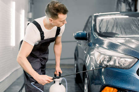Car washing, detailing concept. Car wash service worker cleaning headlights of luxury blue car using high pressure waterの写真素材