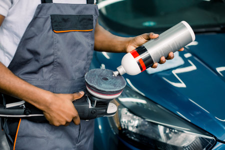 Cropped image of African man, auto service worker, wearing white t-shirt and gray overalls, putting...
