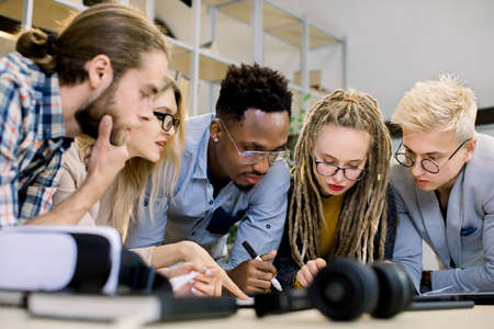 Concentrated diverse multiethnic colleagues gather in office room to brainstorm and discuss financial statistics and joint project together. Office meeting, teamwork concept.の写真素材