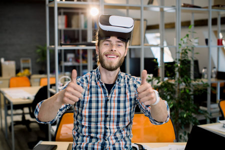 Young smiling creative handsome bearded man working in the office, trying a new product or playing...