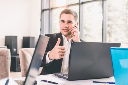 Businessman showing thumbs up while using laptop in office.