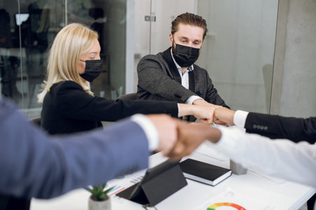 Close up cropped image of happy business coworkers with face protective masks, bumping their fists...