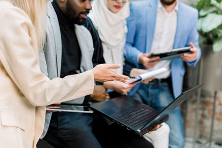Cropped image of team of young multiethnic male and female business people in modern office, working with papers, laptop computer and digital tablet.の写真素材