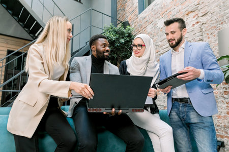 Team of multiethnic smart male and female business people leaning on the blue sofa in modern office,...