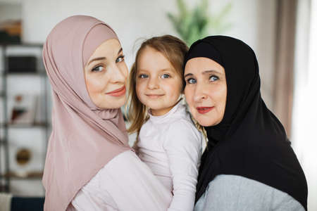 Muslim grandmother, daughter and grandchild together at home, happy domestic life moments. Family having fun, concepts about elderly, mult-generation islamic family and relationshipの写真素材