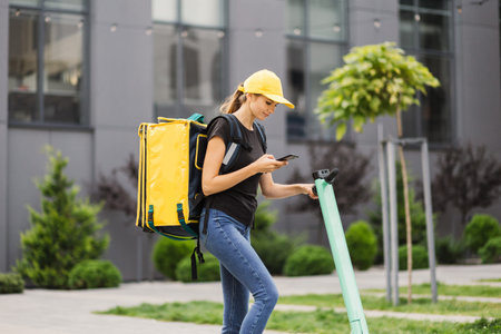 Portrait of female courier with thermo backpack browsing address on mobile phone map standing at...