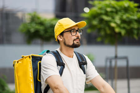 24 hours delivery service from cafes and restaurants. Takeaway, portrait of delivery boy on scooter with yellow isothermal backpack. Courier delivering food on scooter to avoid evening traffic jamsの写真素材