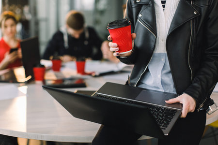 Cropped Portrait Of Successful Business Woman in casual wear Holding red Cup Of Hot Drink In Hand and working on laptop. Young coworkers working together.の写真素材