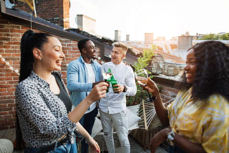 Group of four multiracial people spending leisure time with fun on rooftop. Two women toasting with drinks, two men embracing on background. Party time.の写真素材