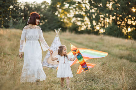 Happy Native American family having fun playing with kite in the field or park together. Pretty boho hippie mother and her little daughter walking with a kite. Little girl holds kite and looks awayの写真素材