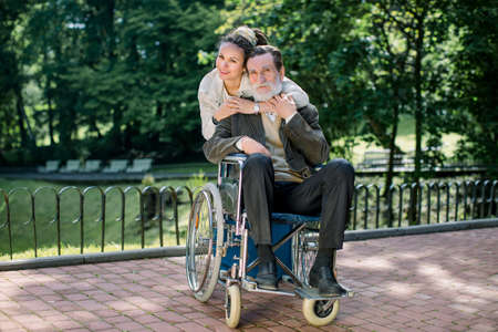Happy granddaughter, nurse, girl with dreadlocks hugging her elderly grandfather in wheelchair, smiling, walking in the park. Concept of care for elderly people, palliative care, boarding house.の写真素材