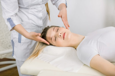Cropped image of hands of young female cosmetologist examining face and hair of pretty blond girl, relaxed lying on the couch. Cosmetology and beauty center, spa procedures. Planning beauty treatment.の写真素材