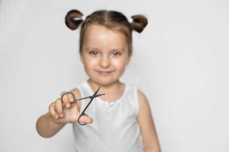 Happy 3 years old kid girl holding scissors for trim childs fingernails, smiling to camera. Baby nails hygiene concept. Close up, isolated on white. Focus on the scissors.の写真素材