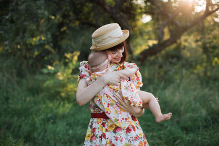 Happy mother and her little daughter in the summer garden. Caring lovely mom holding her cute baby girl on hands and gently huggingの写真素材