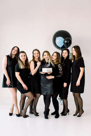 Portrait of beautiful bridesmaids in black dresses with attractive bride-to-be in the middle holding delicious cake. Background is decorated with air balloonsの写真素材