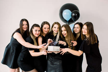 Young happy ladies in black dresses celebrating birthday at studio. Girl best friends having fun holding birthday cake and smiling. Birthday party, holiday, womens day concept.の写真素材