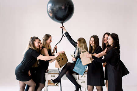 Pretty girl sitting on the vintage table and holding big black balloon. Her beautiful six friends giving presents and having fun. Birthday party concept, holiday.の写真素材