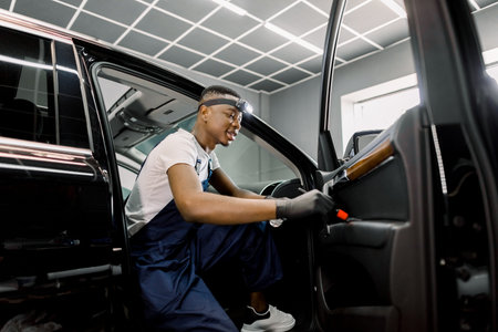 Side view of young African American man worker at car service station, making professional manual...