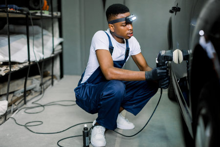 Auto detailing service, polishing of the car. Side view of young African American man worker in...