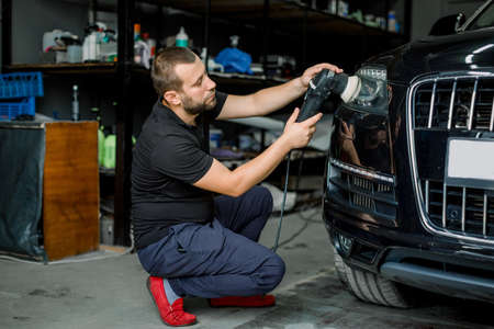 Car detailing series, polishing concept. Professional male auto service worker, waxing and polishing headlight of black car with orbital polish machine.の写真素材