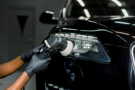 Car wax polishing process. Cropped close up image of hands of male professional African worker in...