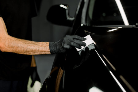 Cropped close up image of male hand in protective black glove, holding white sponge with solid...