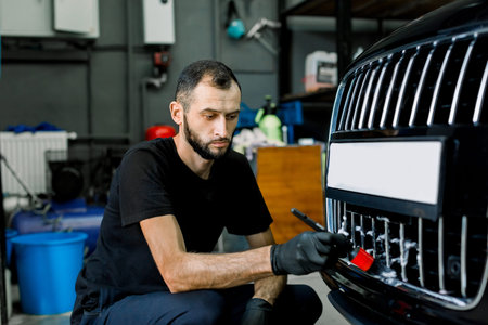 Close up photo of young male worker in black protective gloves cleaning radiator grille in foam with...