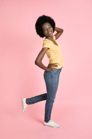 Full length portrait of a cheerful young African American woman with afro hairstyle, wearing jeans...
