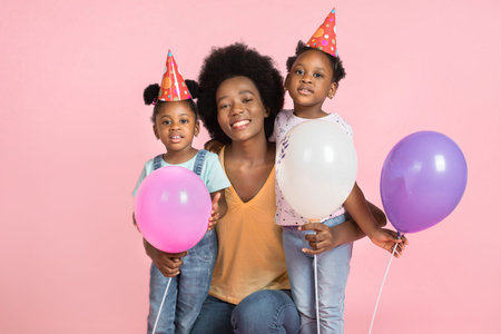 Funny family, African mother and two daughters on a pink background, having fun with colorful air...