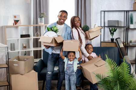 Cheerful afro american family holding boxes while standing at bright modern apartment. Happy family...