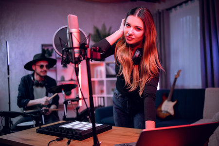 Charming woman in headphones using laptop, microphone and dj controller for creating music in...
