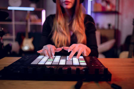 Selective focus of female musician mixing music on dj controller while recording song at studio. Young woman creating new track while sitting at table at dark room.の写真素材