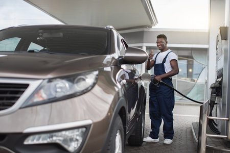 Gas station, transportation and energy concept. African man, professional gas station worker in...