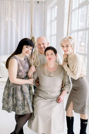 Christmas and New Year holidays. Happy big family, middle aged parents and two young daughters, posing to camera at cozy light decorated room interior with big windows and Christmas treeの写真素材