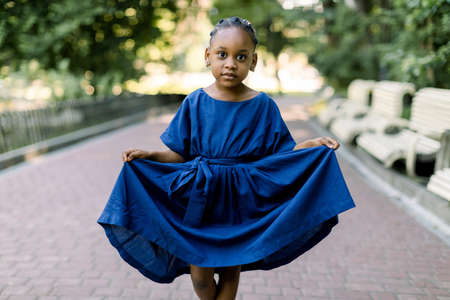 Outdoor portrait of a cute little African child girl in nice blue dress, looking at camera. Playful little dark skinned girl portrait in the park.の写真素材