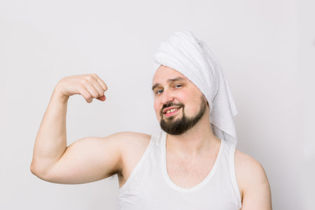 Funny young caucasian man with mustache and beard, with white towel on head, smiling at camera,...
