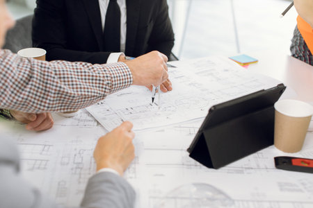 Engineers and designers using modern devices and architect equipments while analysing blueprint of...