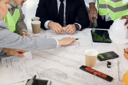 Close up of architects, engineers and designers sitting together at table and analysing blueprints....